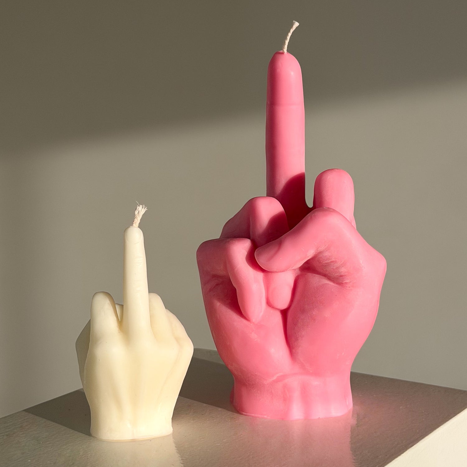 Pink and white candle shaped like middle fingers on a neutral background