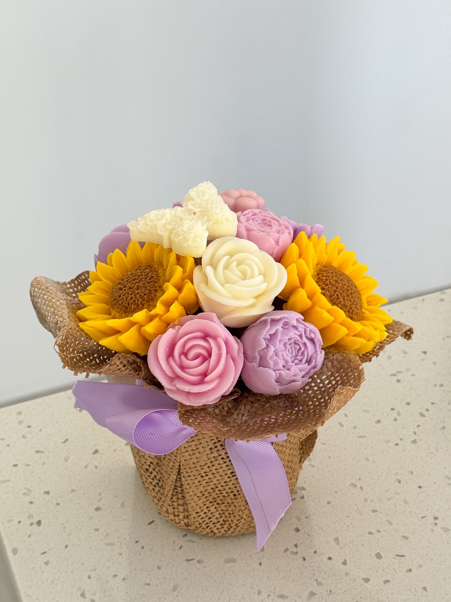 Bouquet of wax flowers with a purple ribbon on a light surface.