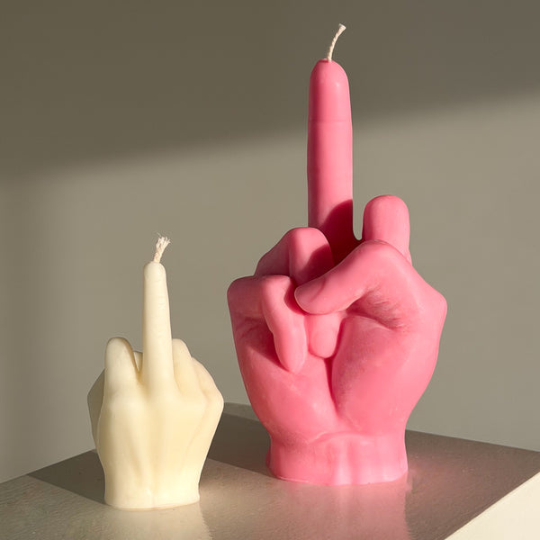 Pink and white candle shaped like middle fingers on a neutral background