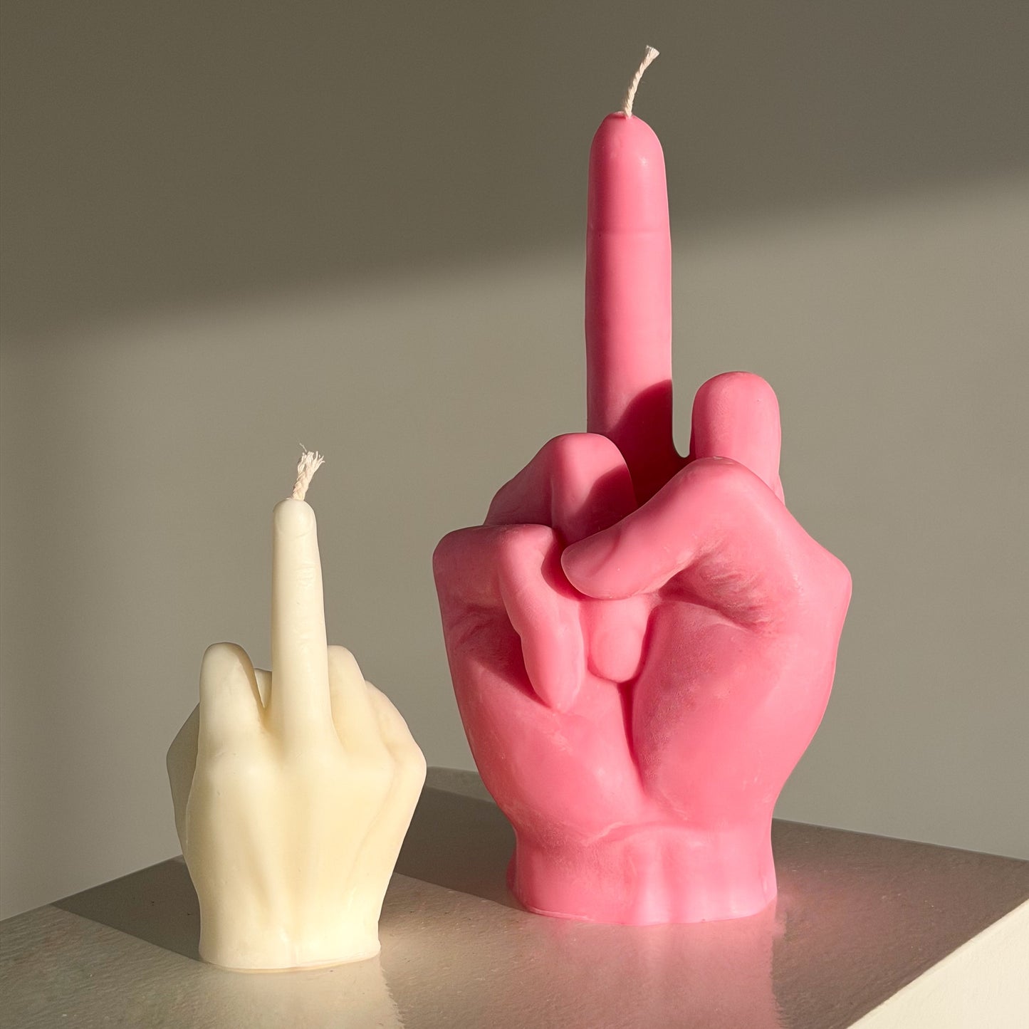 Pink and white candle shaped like middle fingers on a neutral background
