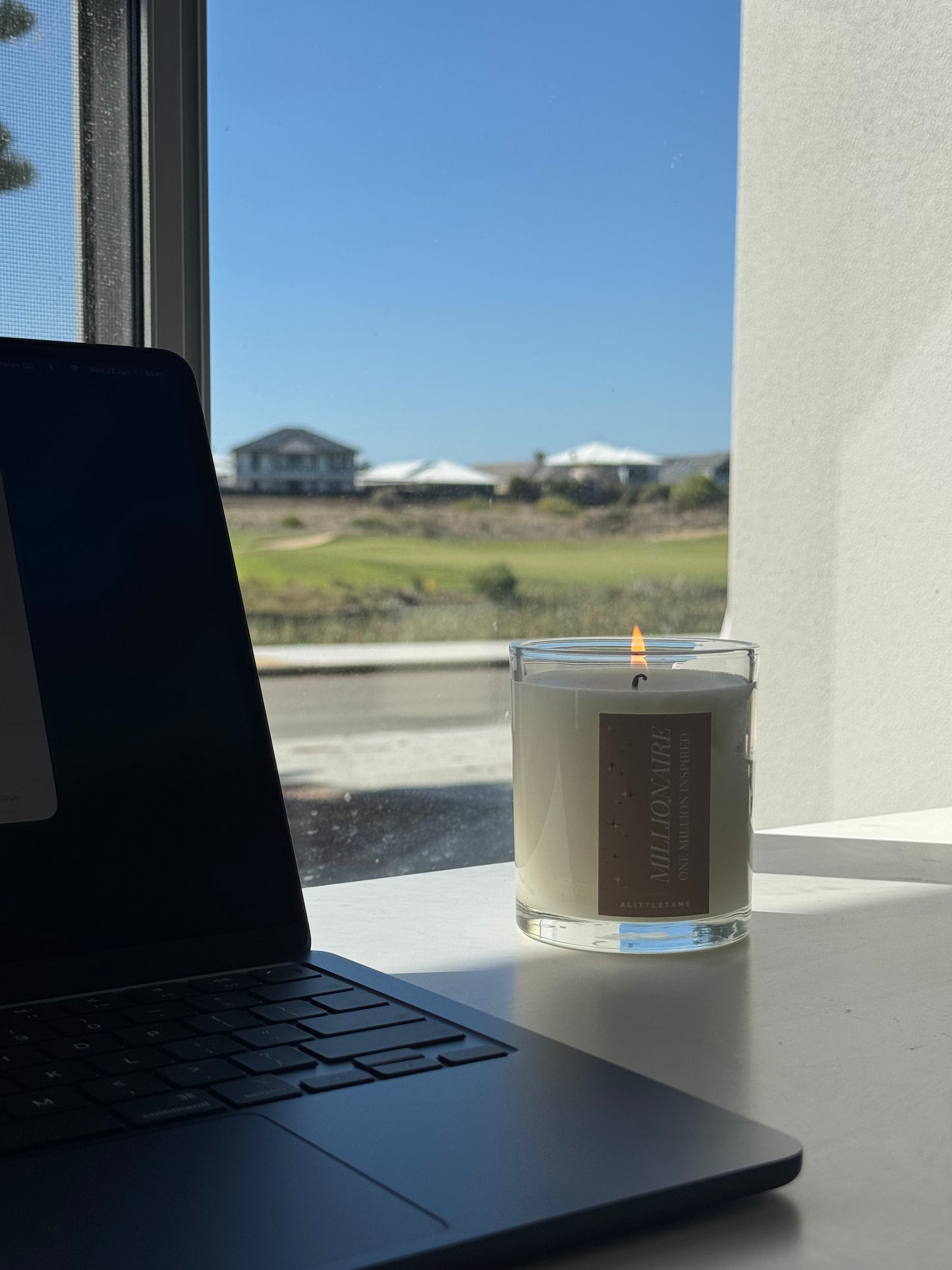 Laptop and candle on a windowsill with a view of houses and greenery.
