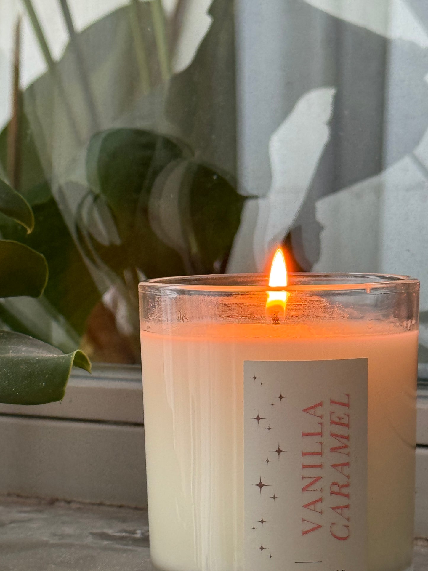 Vanilla caramel candle with a flame, placed indoors with a plant in the background